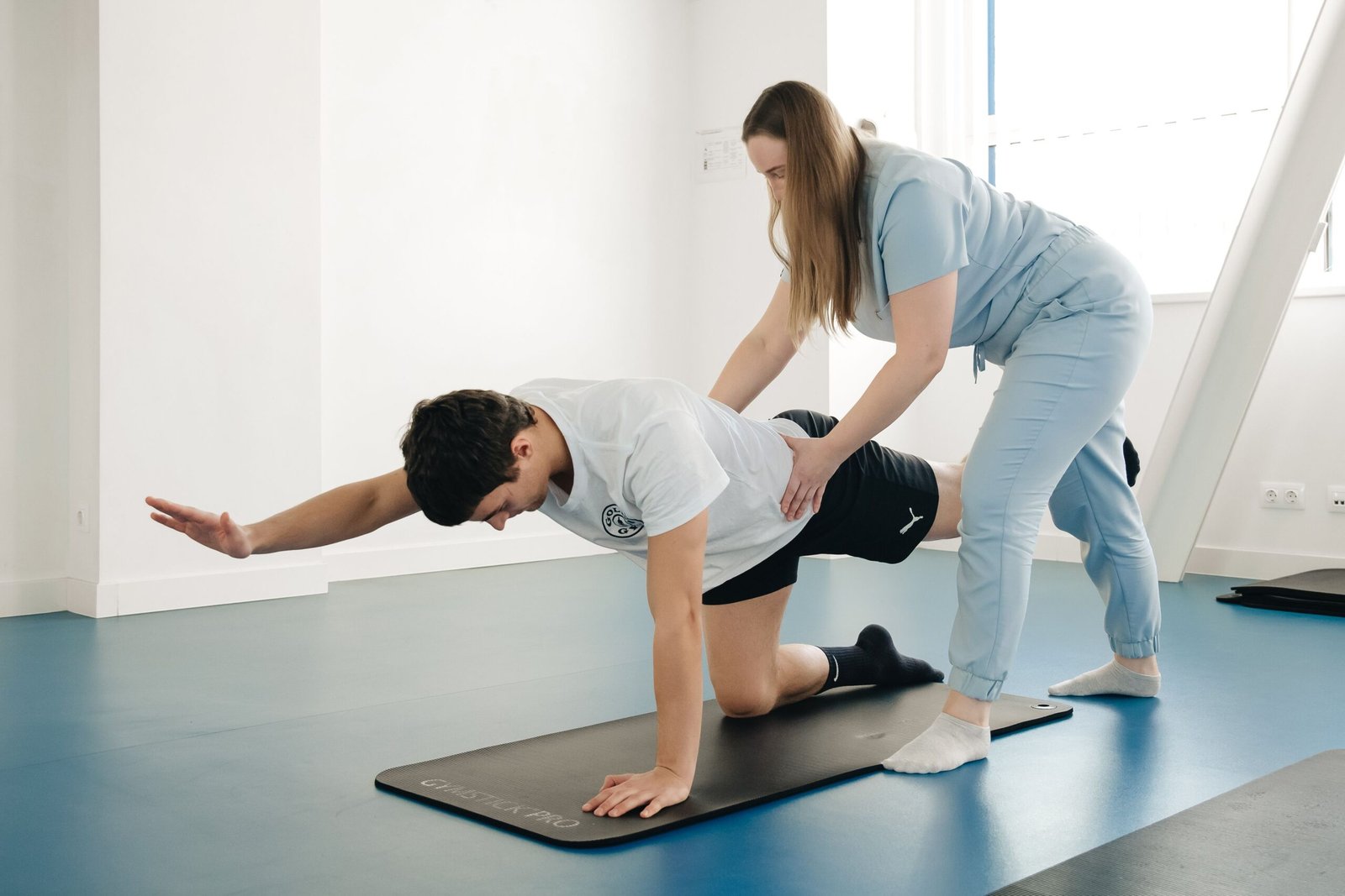A physiotherapist guides a patient's exercise on a mat in a Vilnius gym.